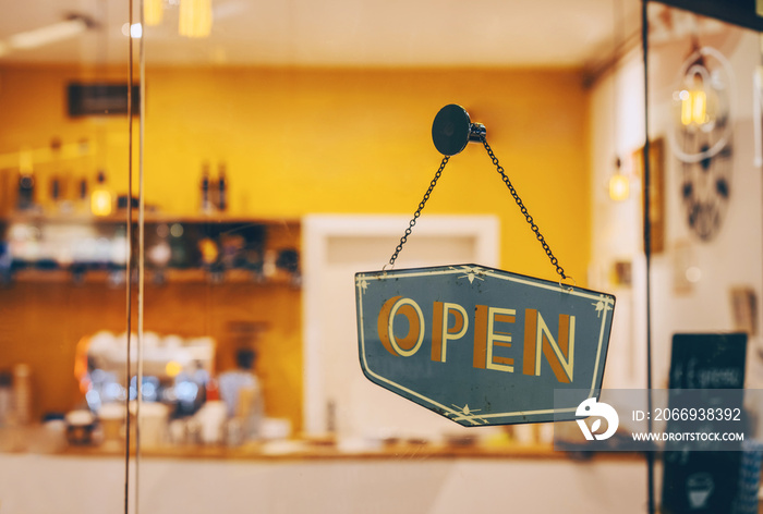 Open sign on glass door in coffee shop, retail store. Local small businesses at food and drink service.