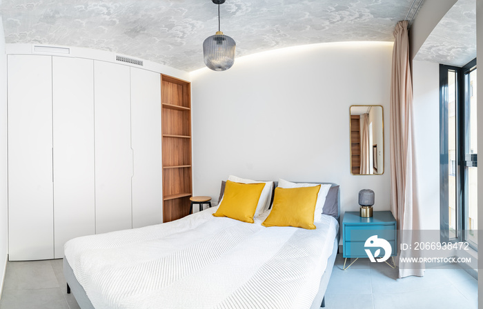 Clean bright bedroom with bed, duvet,side table, lamps,curtain, metal mirror, led indirect light and painted wallpaper on the ceiling. Minimalist white stylish interior with wood and brass details.