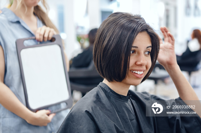 Closeup portrait of hispanic latin girl woman sitting in chair in hair salon looking in mirror at her new haircut, short bob pixie, happy joy emotion