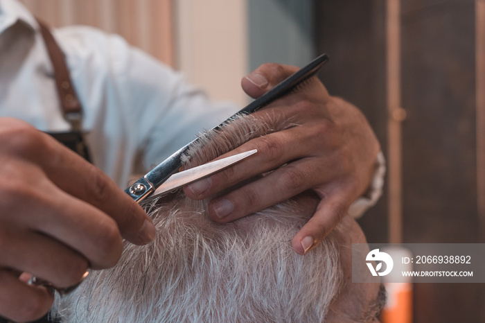 Detalle de mano y tijera cortando cabello a cliente senior en la peluquería.