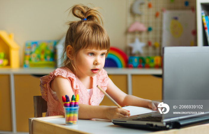 Little girl primary school student drawing or writing watching online lesson using the notebook