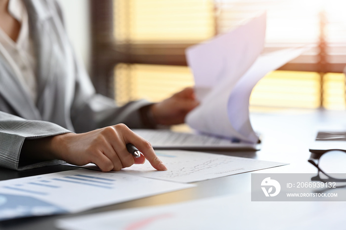 Selective focus on Businesswoman’s hand doing business, graphs and charts being demonstrated on the report with light flare coming through window