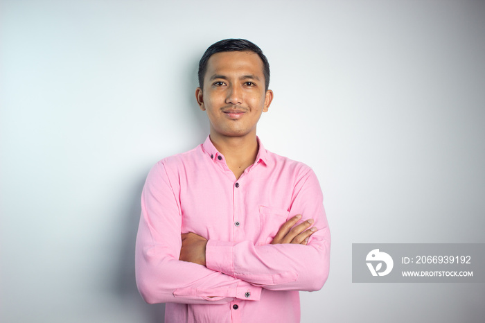 Portrait of confident smiling Asian young man wearing pink shirt standing with arms folded isolated on white background.