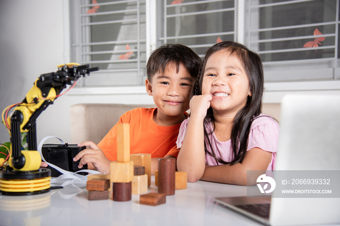 Two children programming and testing robot arm their science, Kid little girl program code to robot with laptop computer and the boy test with remote control to pick up wood block, education lesson