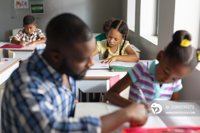 African american young male teacher assisting african american elementary girl studying at desk