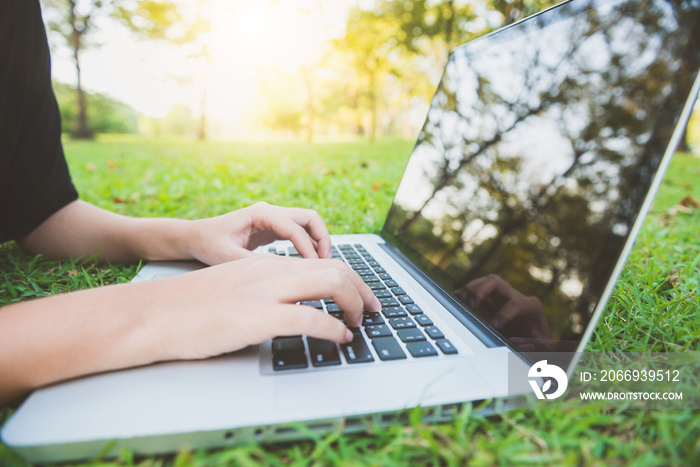 Young asian woman’s legs on the green grass with open laptop. Girl’s hands on keyboard. Distance learning concept. Happy hipster young asian woman working on laptop in park. Student studying outdoors.