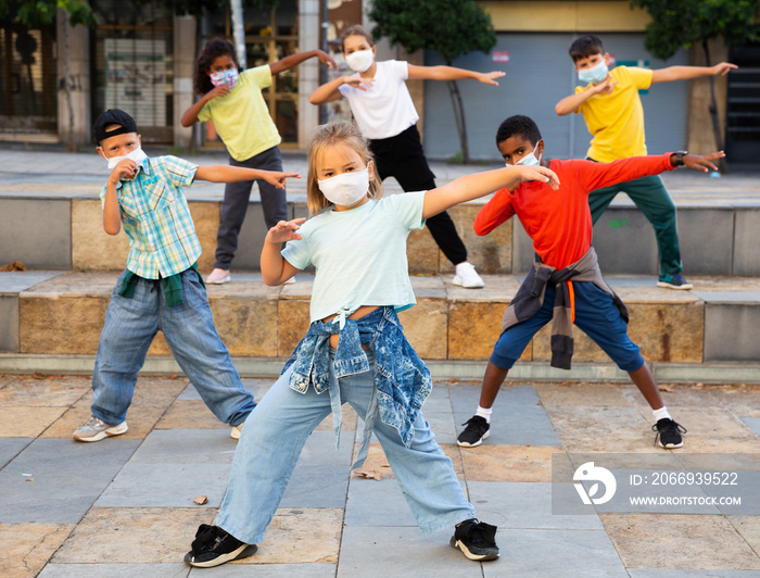 Girls and boys hip hop dancers in protective face masks doing dance workout during open air group class, keeping social distance