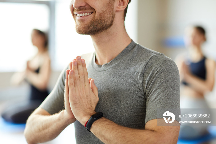 Close-up of smiling young man with stubble wearing smartband holding hands in Namaste while greeting yoga teacher at class