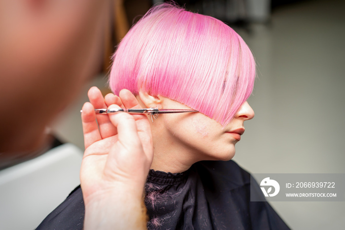 Hand of a hairdresser cutting short pink with scissor hair in a hairdressing salon, close up, side view