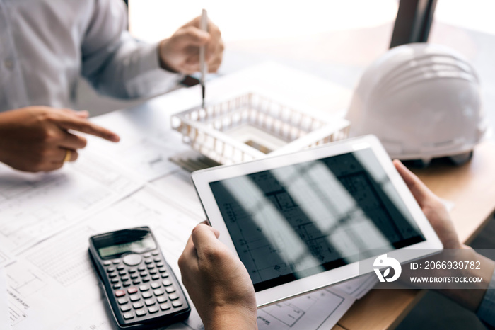 Two engineering working together and using digital tablet looking blueprint and analysis with architectural plan on desk.