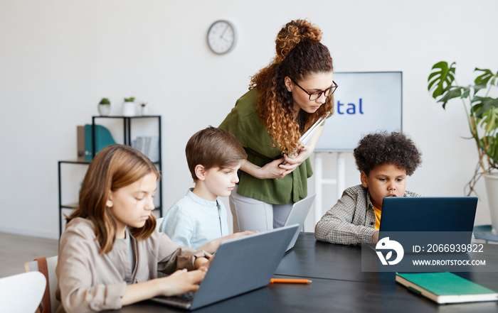 Diverse group of children using computers during IT class in school with young female teacher