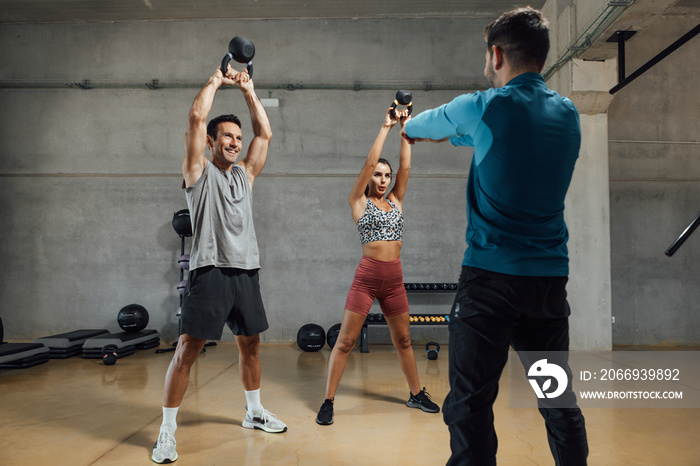 Fitness instructor giving kettle bell class in dark shadow gym