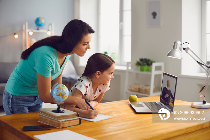 Distance education. Mother and daughter watching online video conference with mature teacher on laptop at home