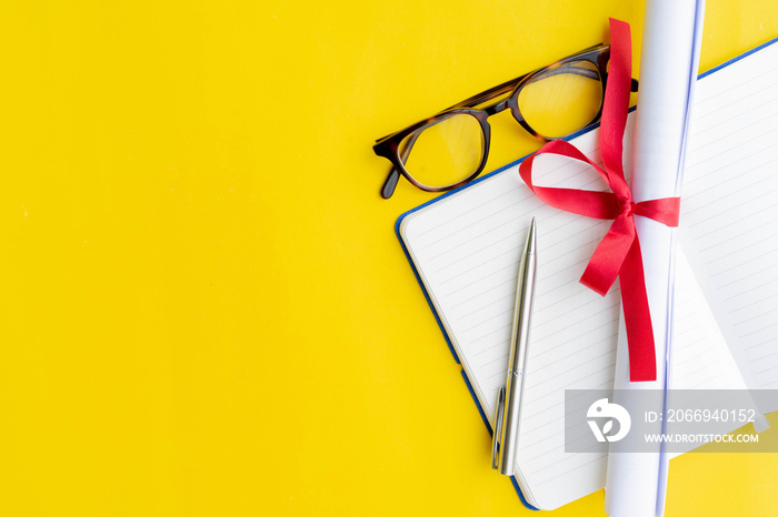 close up top view of certificated degree with notebook and pen and glasses on yellow background for education concept