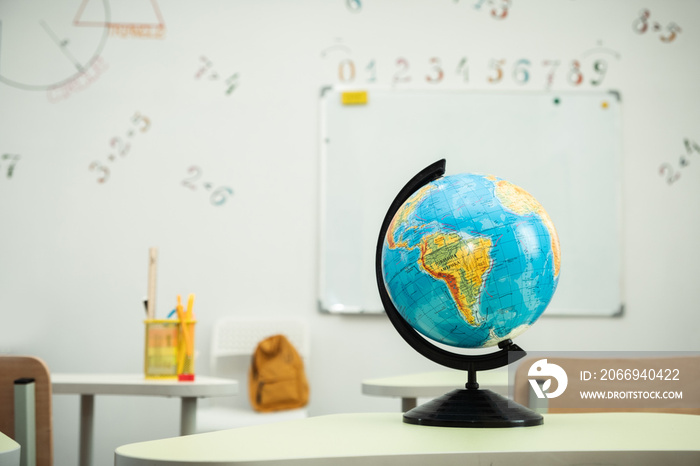 The Globe stands on the desk in the school classroom against the white school board. Planet Earth. Back to school concept. Classroom interior design