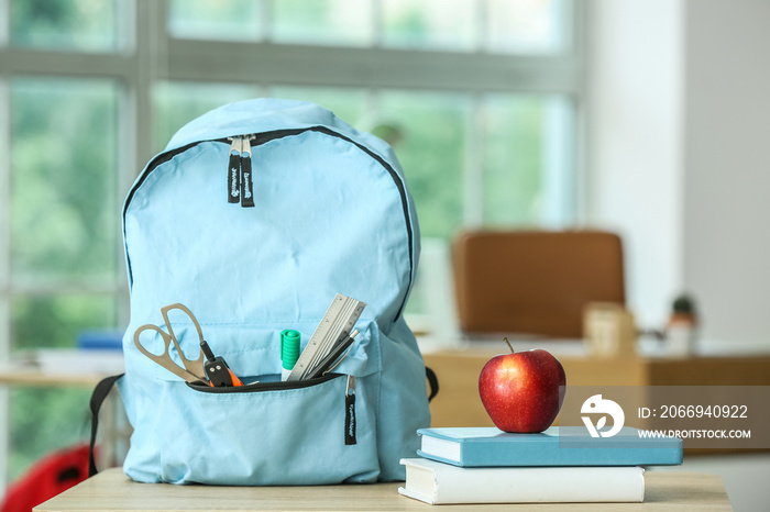 Apple with school books and backpack on table in classroom