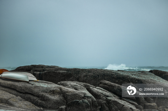 Crashing wave onto rocks  with boats on a misty overcast day.