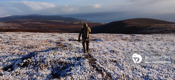 Hunter with rifle in winter landscape in the scottish highlands