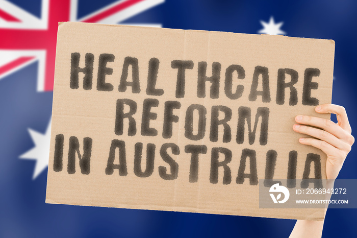 The phrase   Healthcare reform in Australia   on a banner in men’s hand with blurred Australian flag on the background. Nation. Crisis. Problem. Medical help. Reformation. Clinical