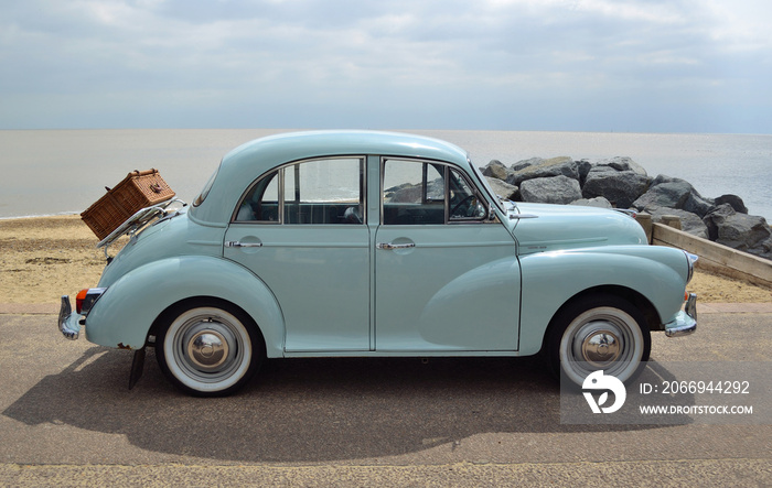 Classic Light Blue Morris Minor with picnic basket parked on seafront promenade.