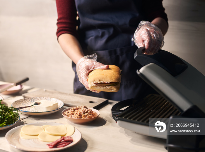 Using special grill equipment in cooking original american street popular food. Detailed of chef baking gourmet sandwich. Process of cooking typical italian refreshments. Gray background. Side view.