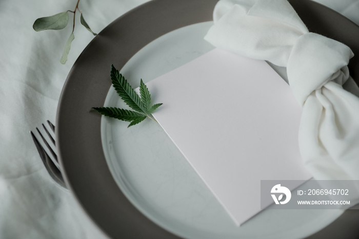 Cannabis friendly dinner concept. Beautiful dinner setup with marijuana leaves and a note for menu. Copy space.