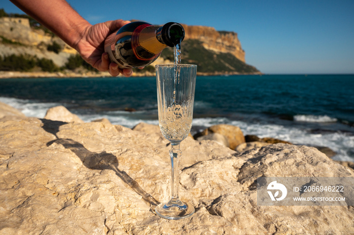 Pouring of French champagne sparkling wine in glass and view on beach and mountains in Cassis, Provence, France