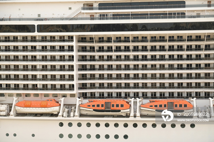 Close-up side view of large white passenger cruise line ship with many round cabin windows, balcony and orange lifeboats.