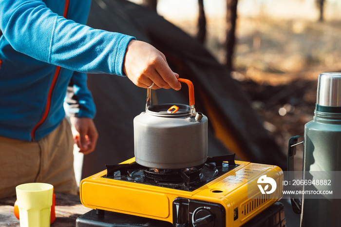 Hand lighting fire at campsite plate for cooking, making tea or coffee. Outdoor food drink item set. Travel tools, camping equipment. Nature picnic rest. Campfire kettle, thermos with hot beverage.