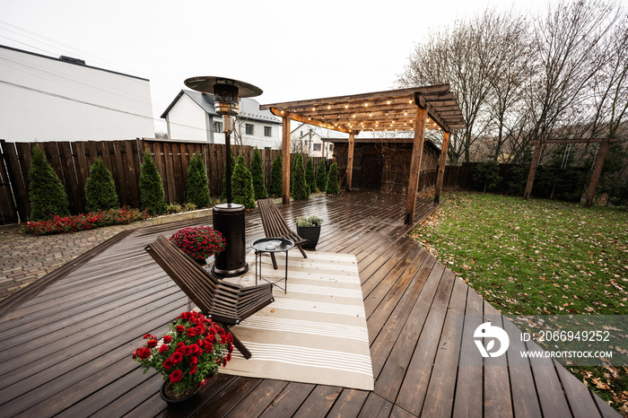 Stainless steel metal gas outdoor patio heater with wooden chairs and pot with flowers at wet terrace. Place to relax.