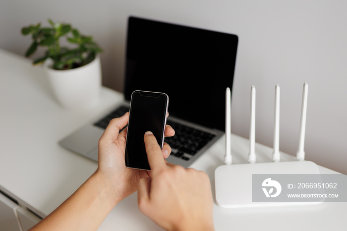 wifi connection concept - hand with phone in the foreground and computer with router on background