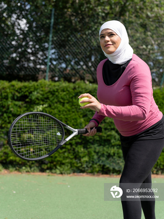 UK,Sutton,Woman in headscarf playing tennis in park