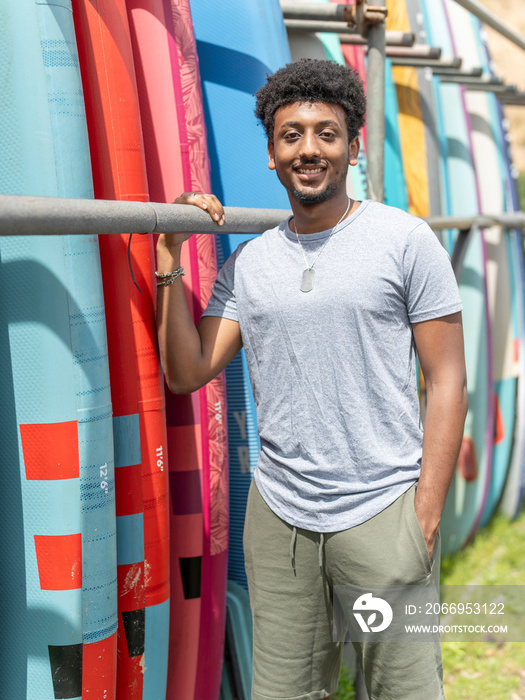 Portrait of smiling man standing next to paddleboard rack