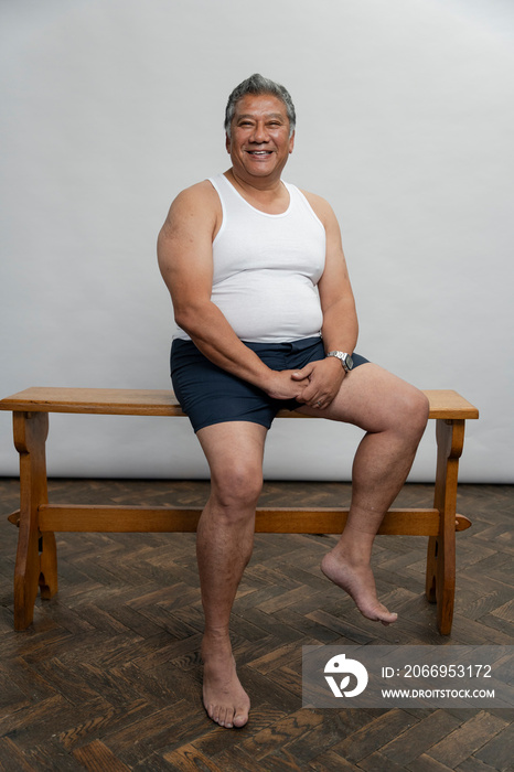 Portrait of smiling senior man sitting on wooden bench against gray background