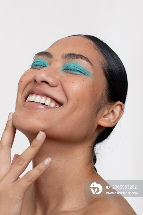 Portrait of smiling woman with black hair and blue makeup on closed eyes