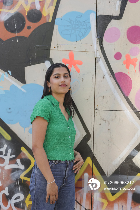 Portrait of young woman standing in front of graffiti wall