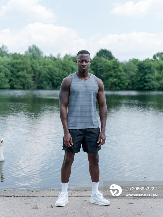 Portrait of muscular man in sports clothing standing by lake