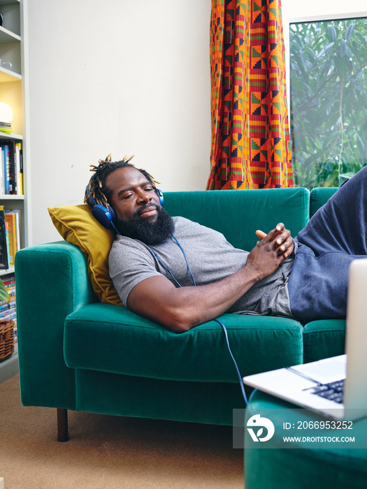 Man lying on sofa, listening to music from laptop