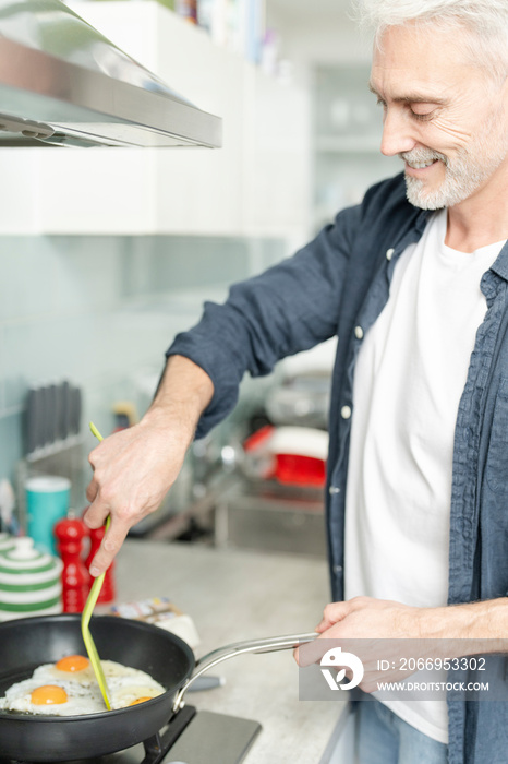 Smiling mature man cooking eggs in pan