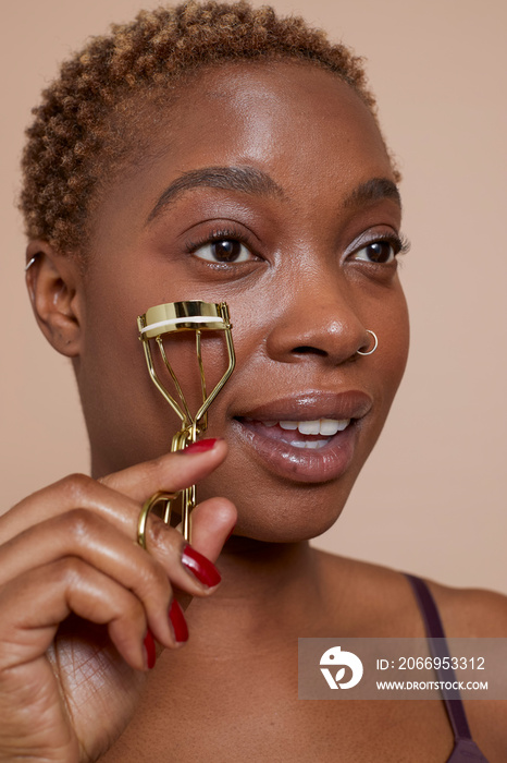 Studio portrait of woman using eyelash curler