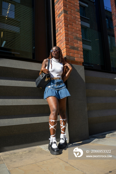 Woman wearing mini skirt,white top and sunglasses leaning on building