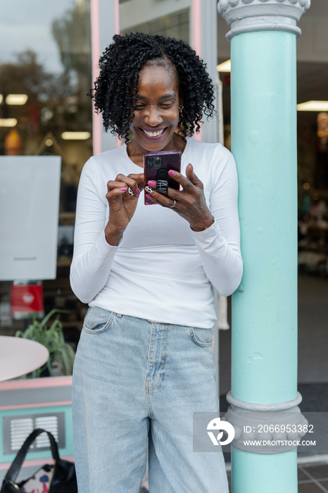 Smiling woman using smart phone in front of building