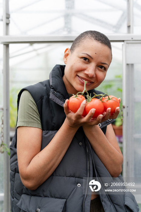 Portrait of smiling woman holding tomatoes in greenhouse