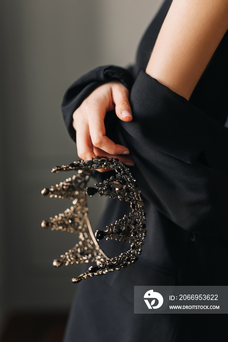 Closeup of a woman in black jacket, holding a black crown in one hand.