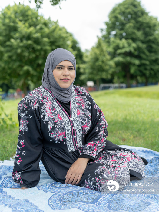 UK,Sutton,Portrait of woman in headscarf sitting on lawn in park