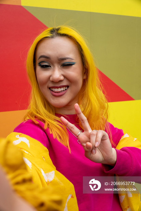 Portrait of young woman with yellow hair showing peace sign