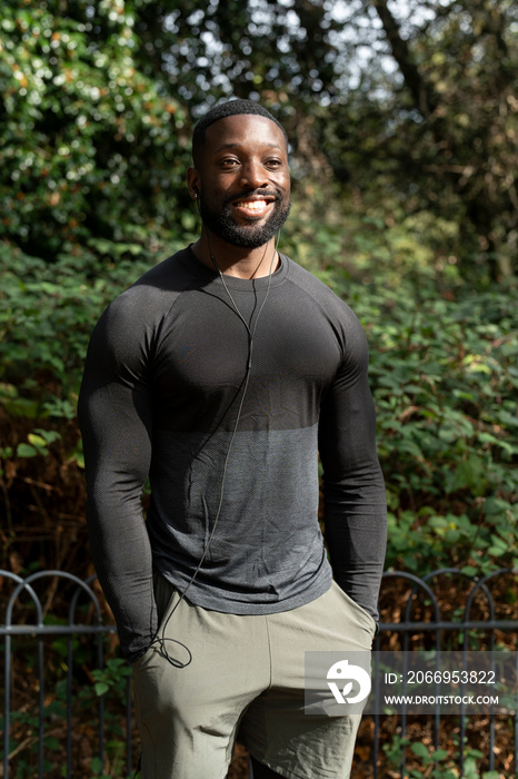 Portrait of smiling athletic man with earbuds standing in park