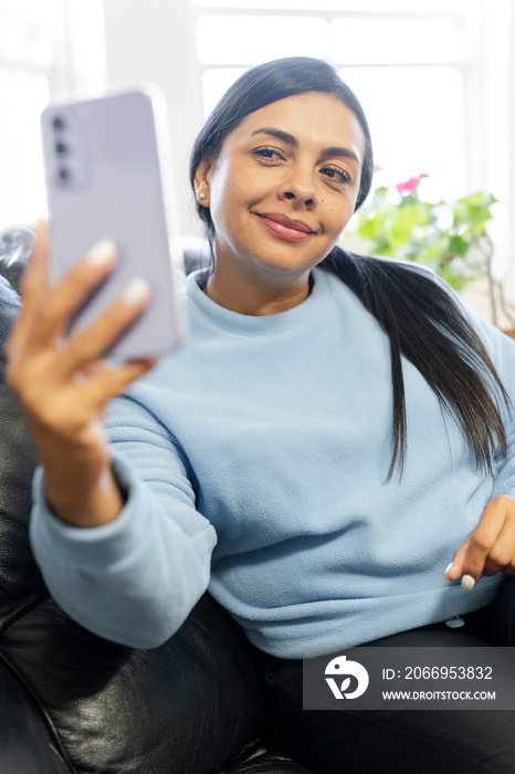 Woman sitting on sofa and using smartphone to take selfie