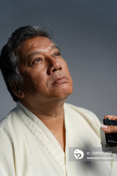 Portrait of serious man putting on perfume against gray background