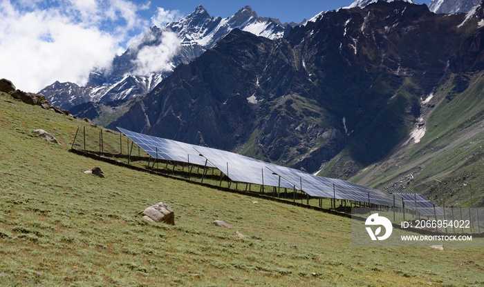 Field with rows of blue solar panels in grassland with snow peak background in Jammu-Kashmir,India